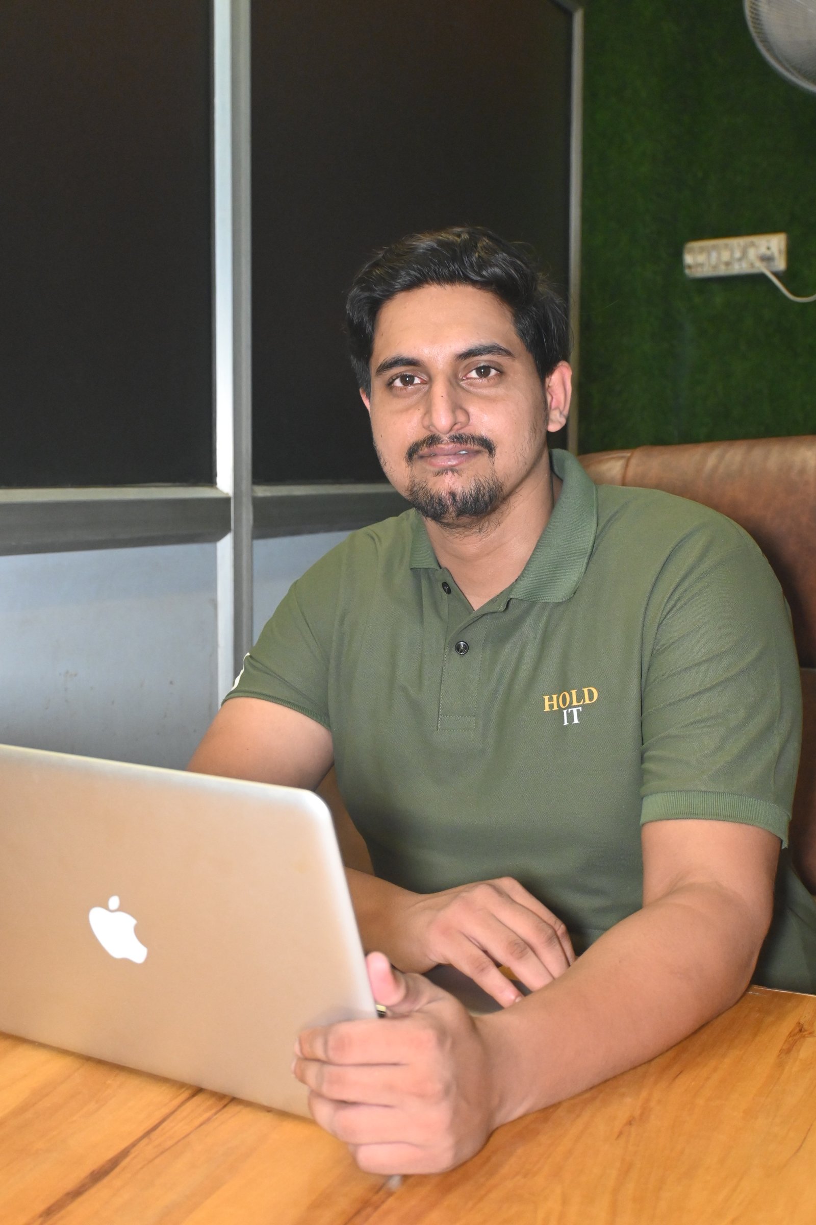 Portrait of Sandeep Gupta in formal wear sitting at a desk with laptop and orange curtain background